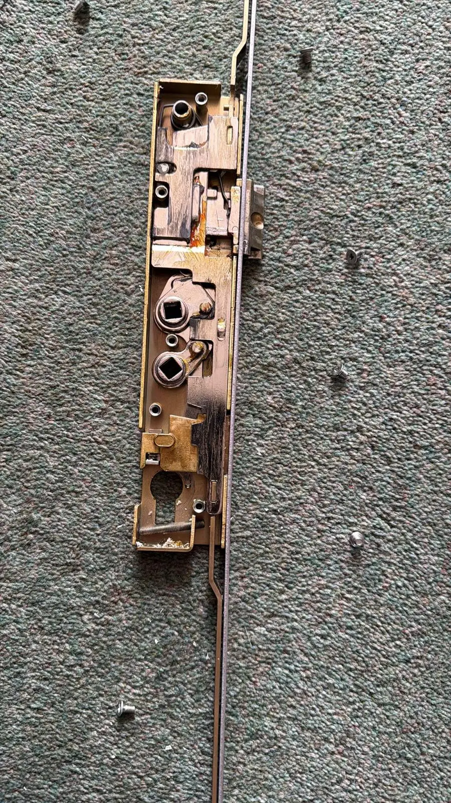 A multipoint lock mechanism removed from a door, lying on carpet