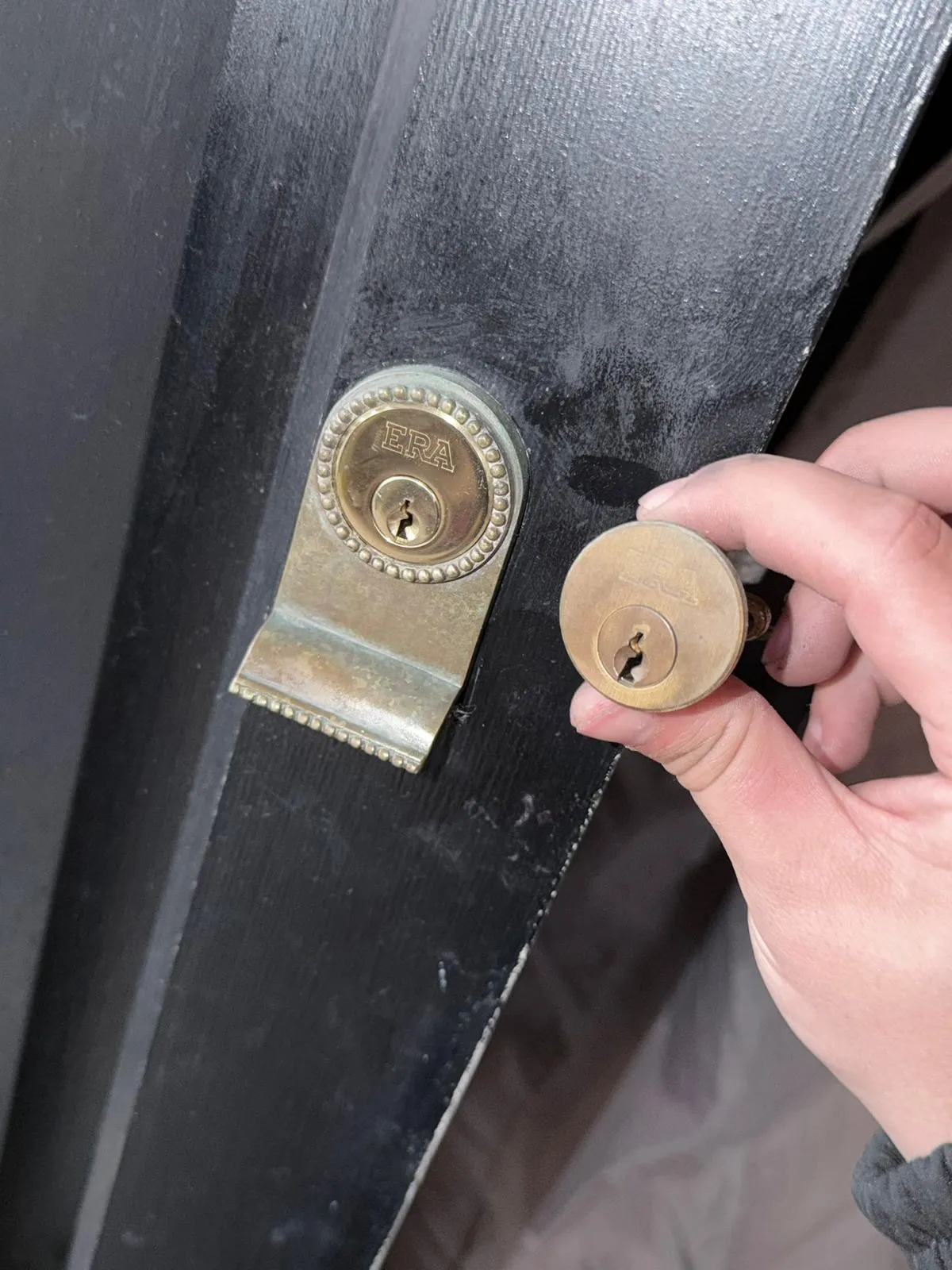 A brass lock cylinder being fitted to a black front door